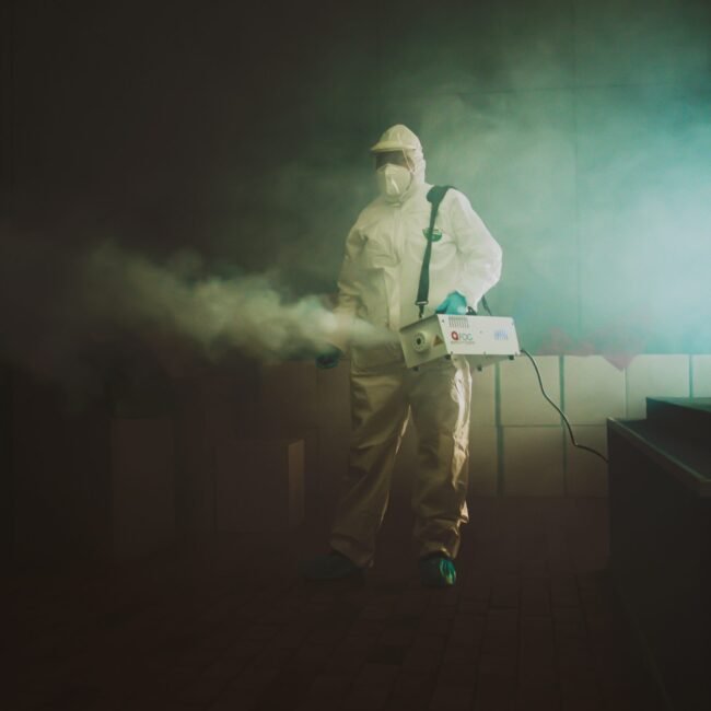 Man in biohazard suit fogging area.