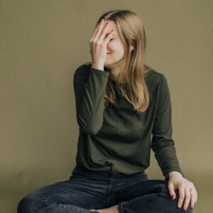 Woman sitting cross-legged on floor covering face.