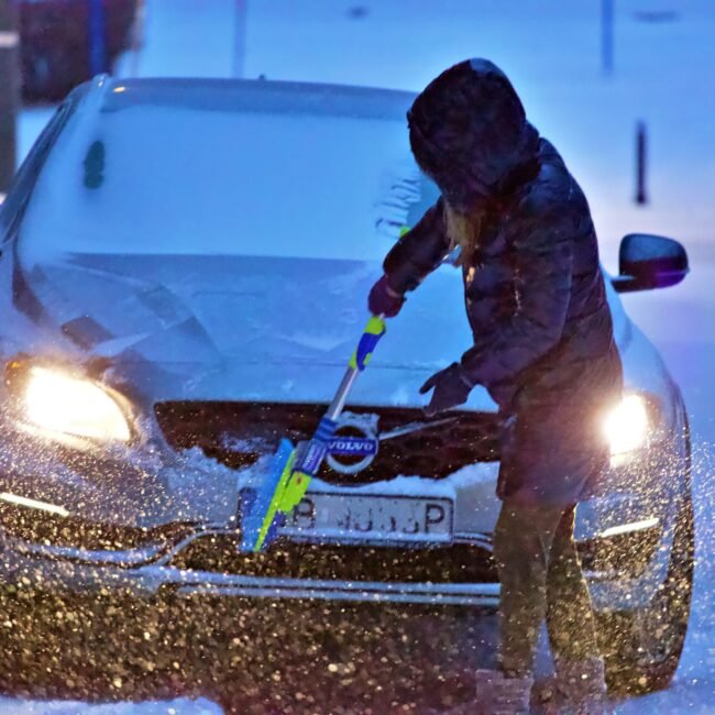 Woman brushing snow off of car.